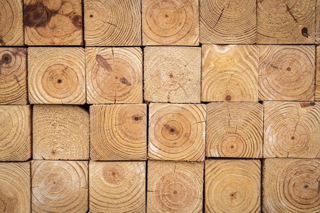 End profile view of stacked 4-inch x 4-inch wood timber, showing the rough edge and wood grain in a lumberyard